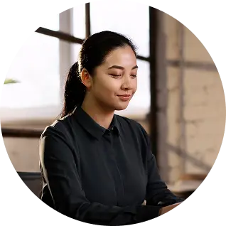 Woman with dark hair tied back, wearing a black shirt, sitting indoors with closed eyes and a slight smile.