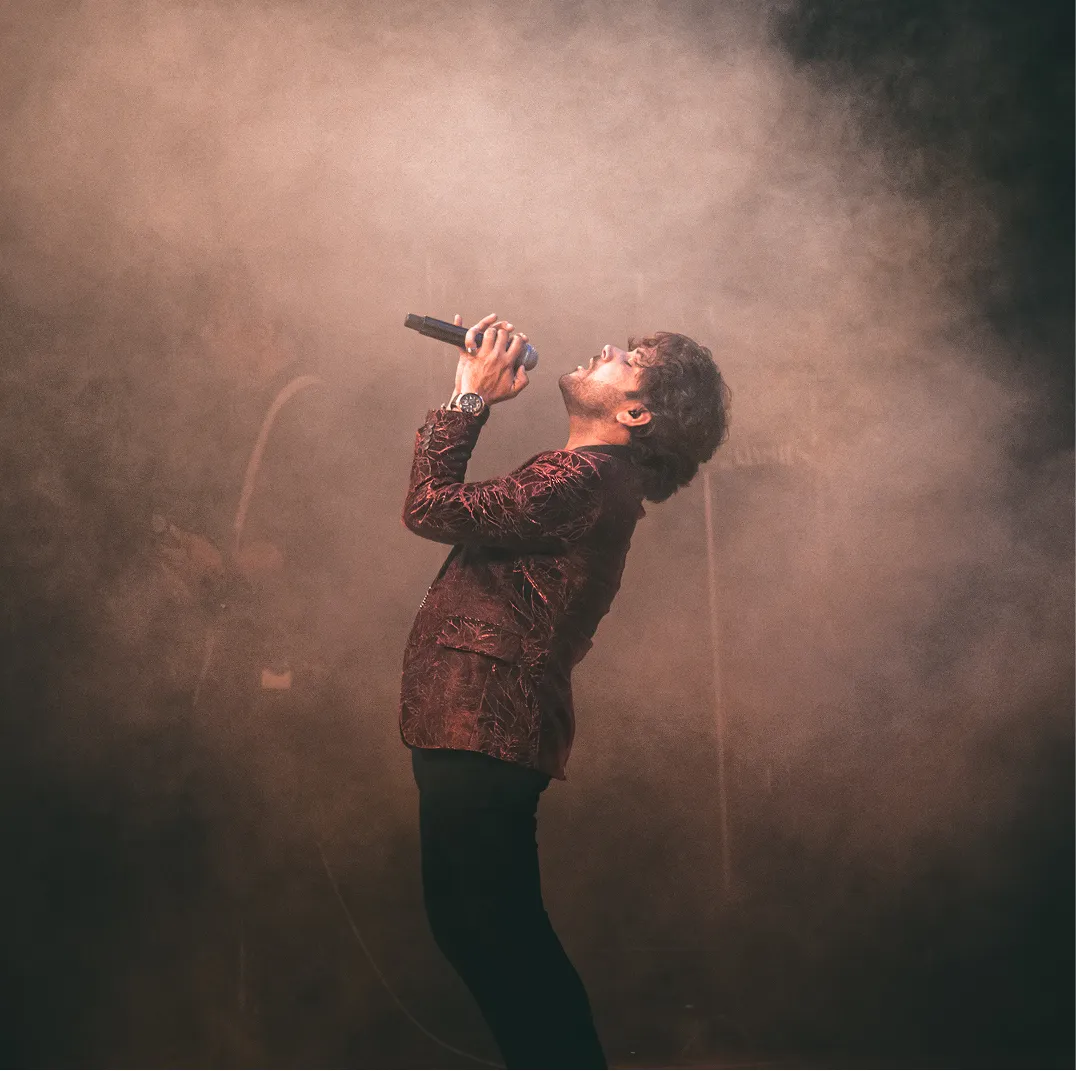 Man passionately singing into a microphone on a smoky stage.